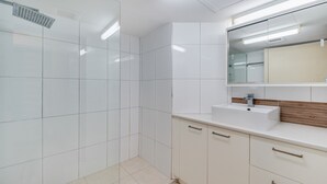 Un baño moderno con azulejos blancos, un lavabo con espejo y zona de ducha.