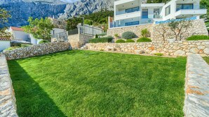 Une villa moderne avec une façade en pierre, une pelouse bien entretenue et un paysage montagneux en arrière-plan.