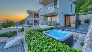 Une maison moderne à deux étages, dotée d’une piscine, d’un jacuzzi et d’un escalier menant à une terrasse.