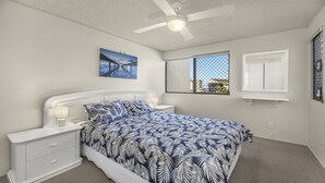 A bedroom with a bed, a nightstand, a ceiling fan, a window with a view, and a door. - Sealanes Unit 8 Kings Beach QLD (KINGS BEACH)
