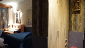 Quarto com cama, mesa de cabeceira, guarda-roupa de madeira e um pequeno banquinho.