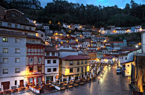 Una calle empedrada flanqueada por edificios, algunos con mesas al aire libre y sombrillas, señal de una zona de restauración.