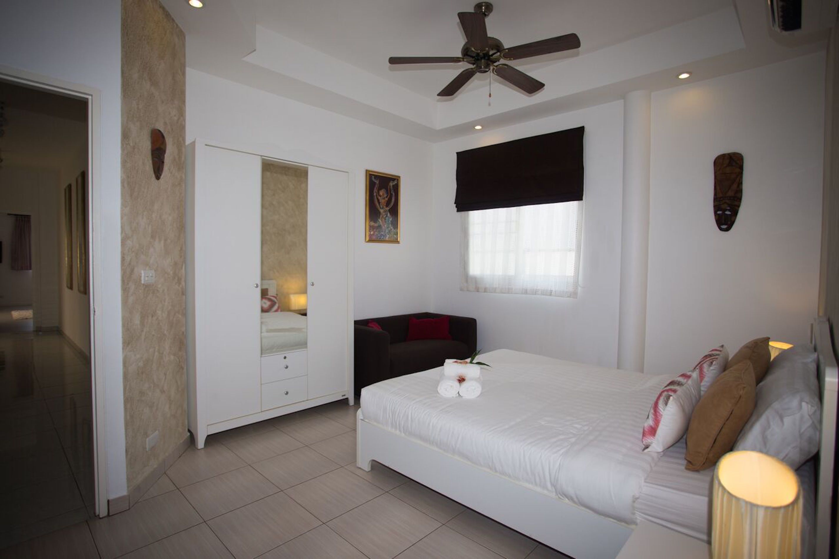 A bedroom with a bed, a ceiling fan, a wardrobe, a window with curtains, and a wall-mounted artwork.