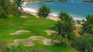 En golfbana med sandbunkrar, palmer och utsikt över havet.