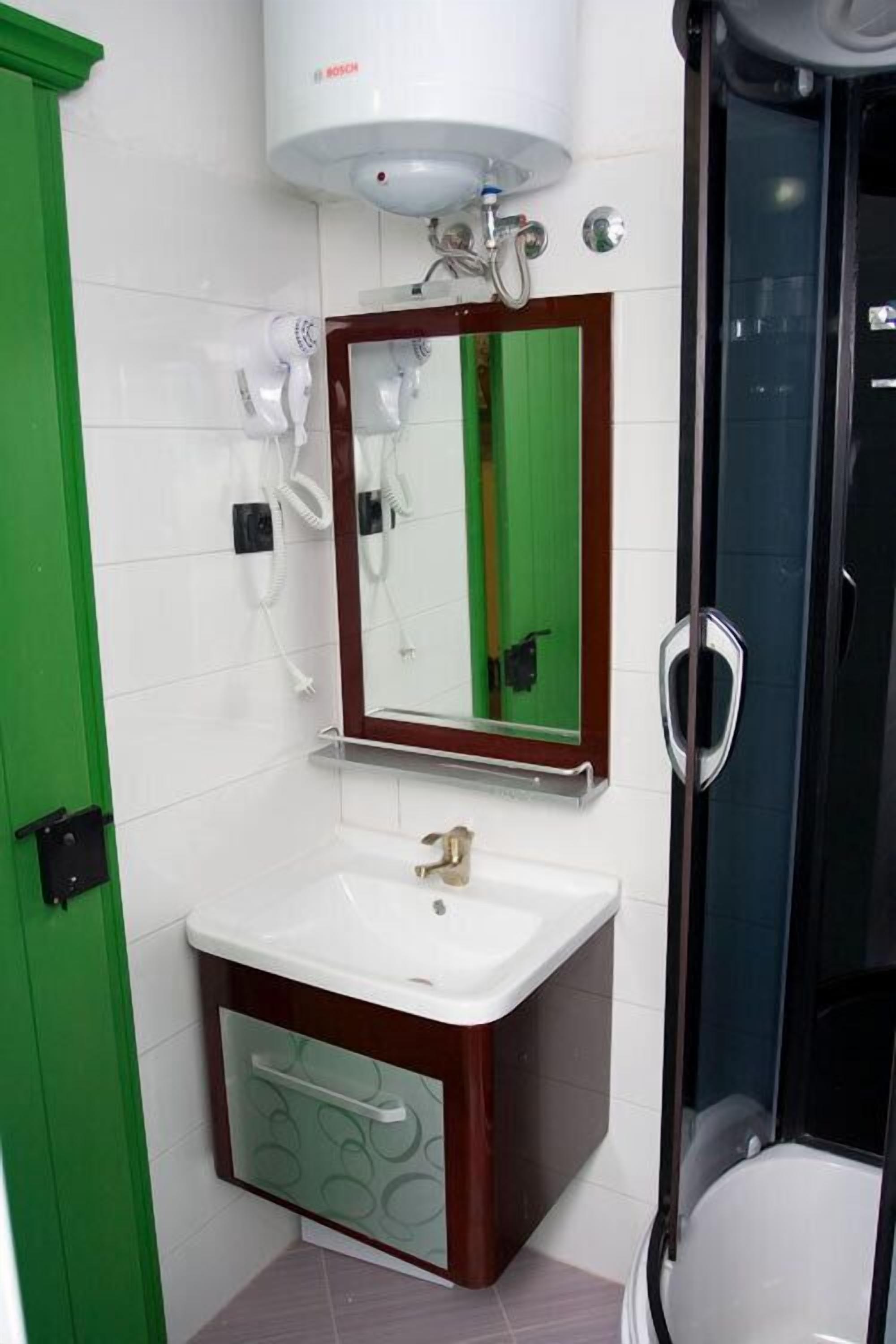 Un baño con un lavabo blanco, un espejo, un calentador de agua Bosch y una ducha con mampara de vidrio.