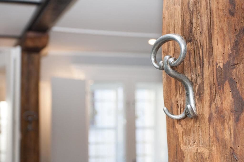 Un gancho metálico sujeto a un poste de madera, probablemente parte de un marco de puerta o ventana.