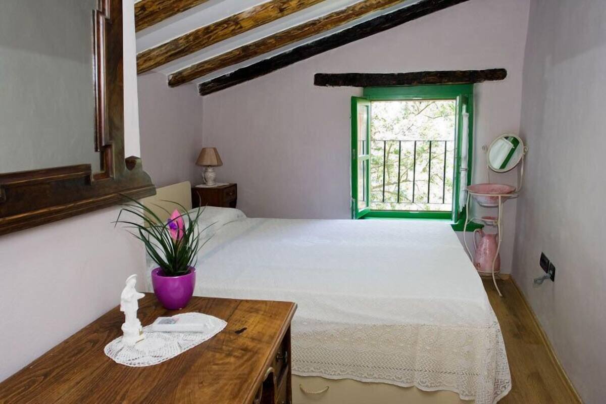 A bedroom with a wooden bed, a nightstand, a dresser, a mirror, a potted plant, and a window with a green frame.