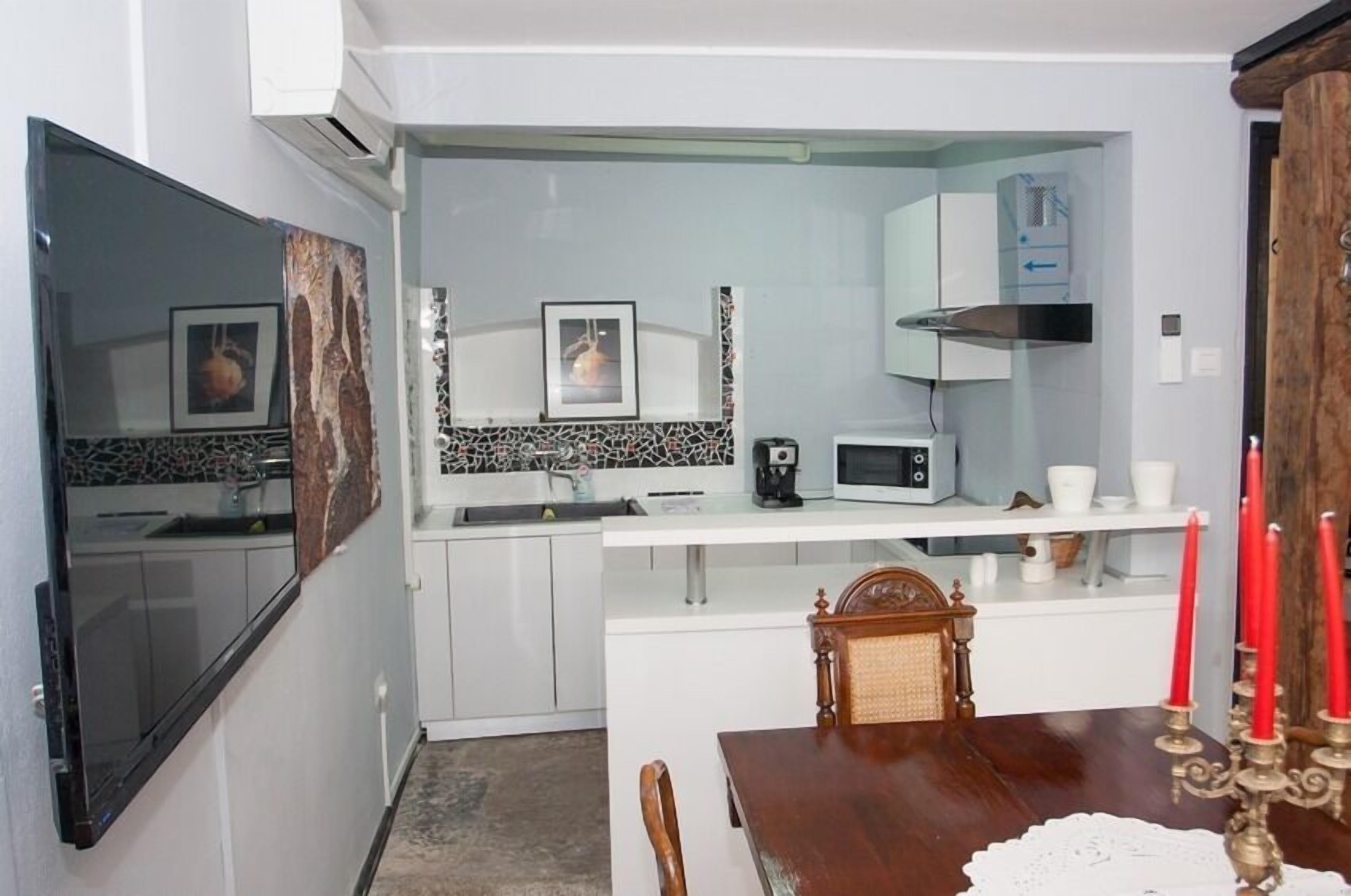 A compact kitchen with white cabinets, a microwave, and a coffee maker. There is a dining table with a candle holder and a chair.