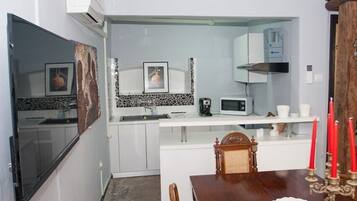 A compact kitchen with white cabinets, a microwave, and a coffee maker. There is a dining table with a candle holder and a chair.