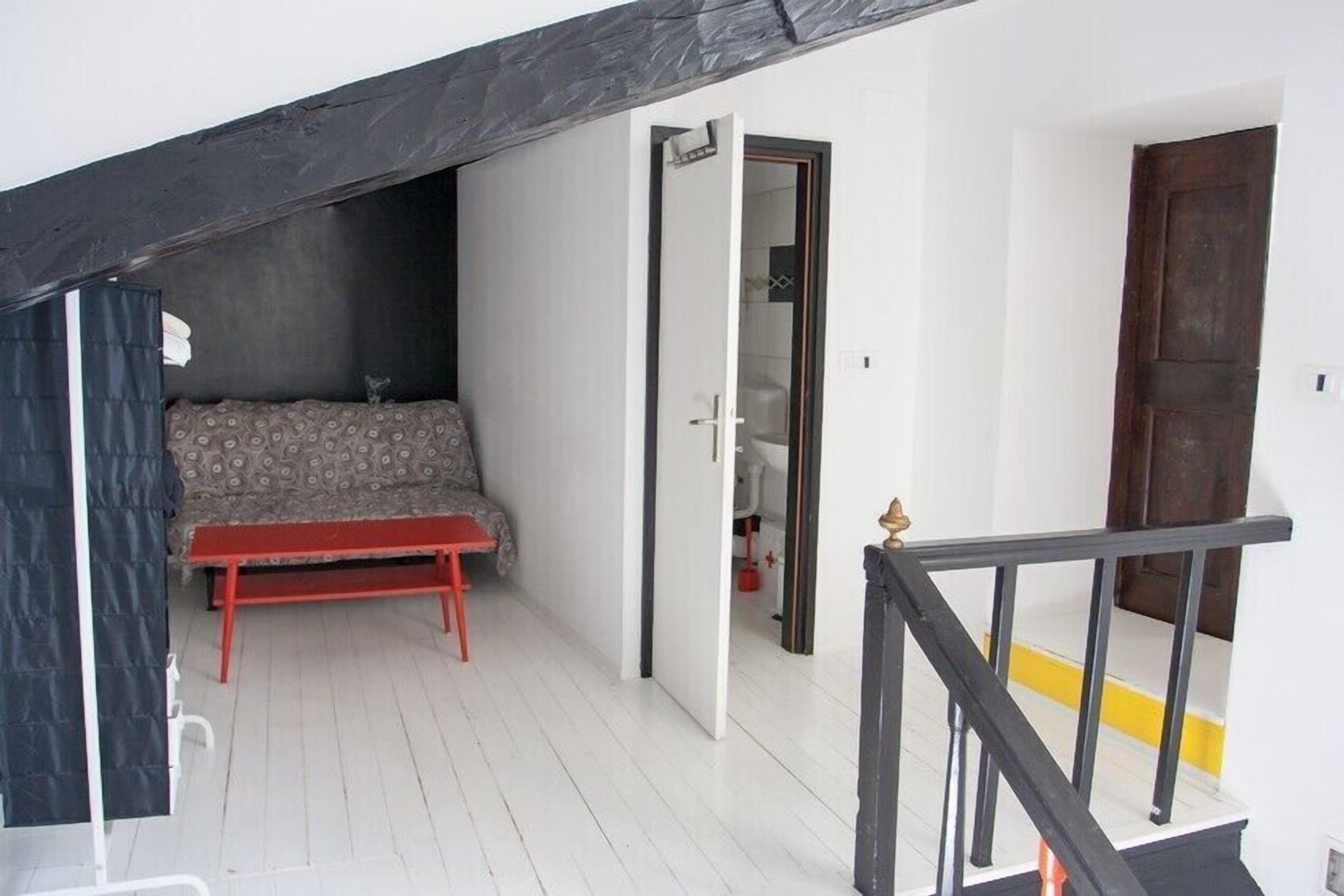 Una habitación pequeña con cama, un banco y una puerta que da a un baño.