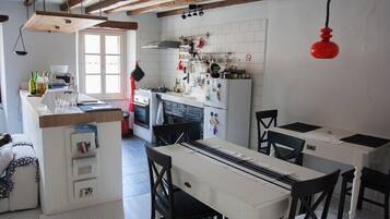 Una cuina amb una illa central, bigues de fusta, un penjoll vermell i una finestra.
