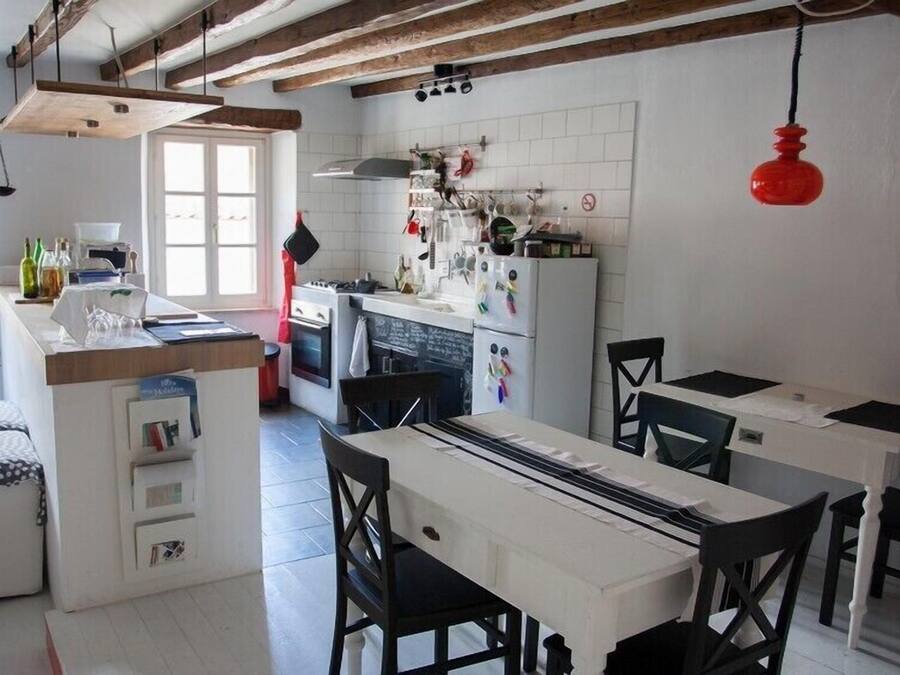 Une cuisine dotée d’un îlot central, de poutres en bois, d’une suspension rouge et d’une fenêtre.
