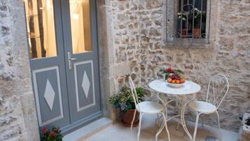 Un muro de piedra con una ventana, una puerta y una pequeña zona exterior con una mesa y dos sillas.
