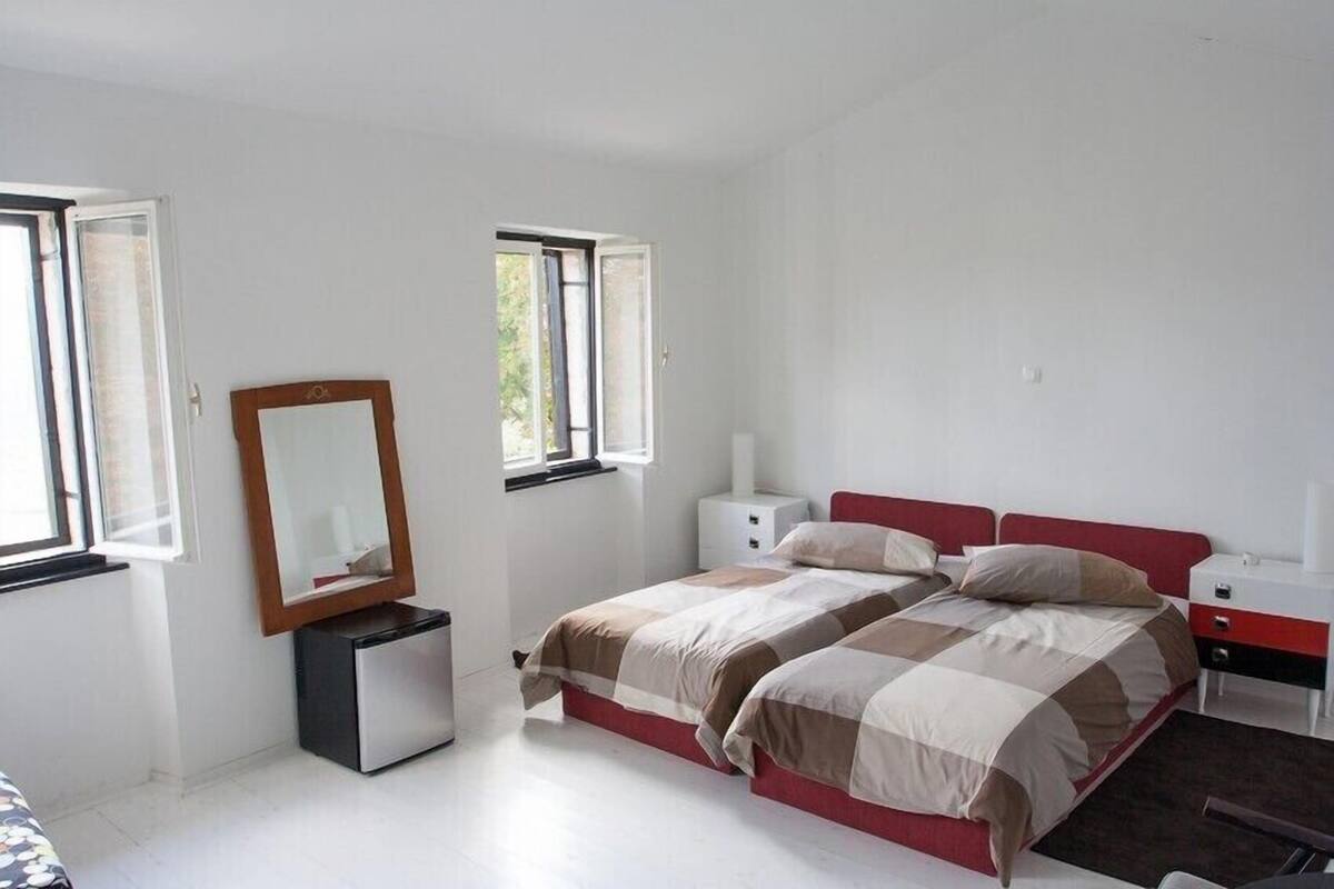A bedroom with two beds, a mirror, a small desk, and a window.