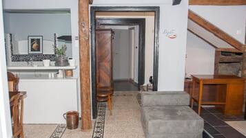 Una habitación con kitchenette, un sofá gris, un armario de madera y una escalera.
