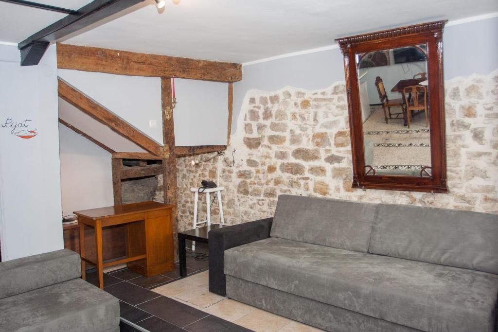A cozy living room with a stone wall, wooden beams, a grey sofa, a wooden table, and a mirror.