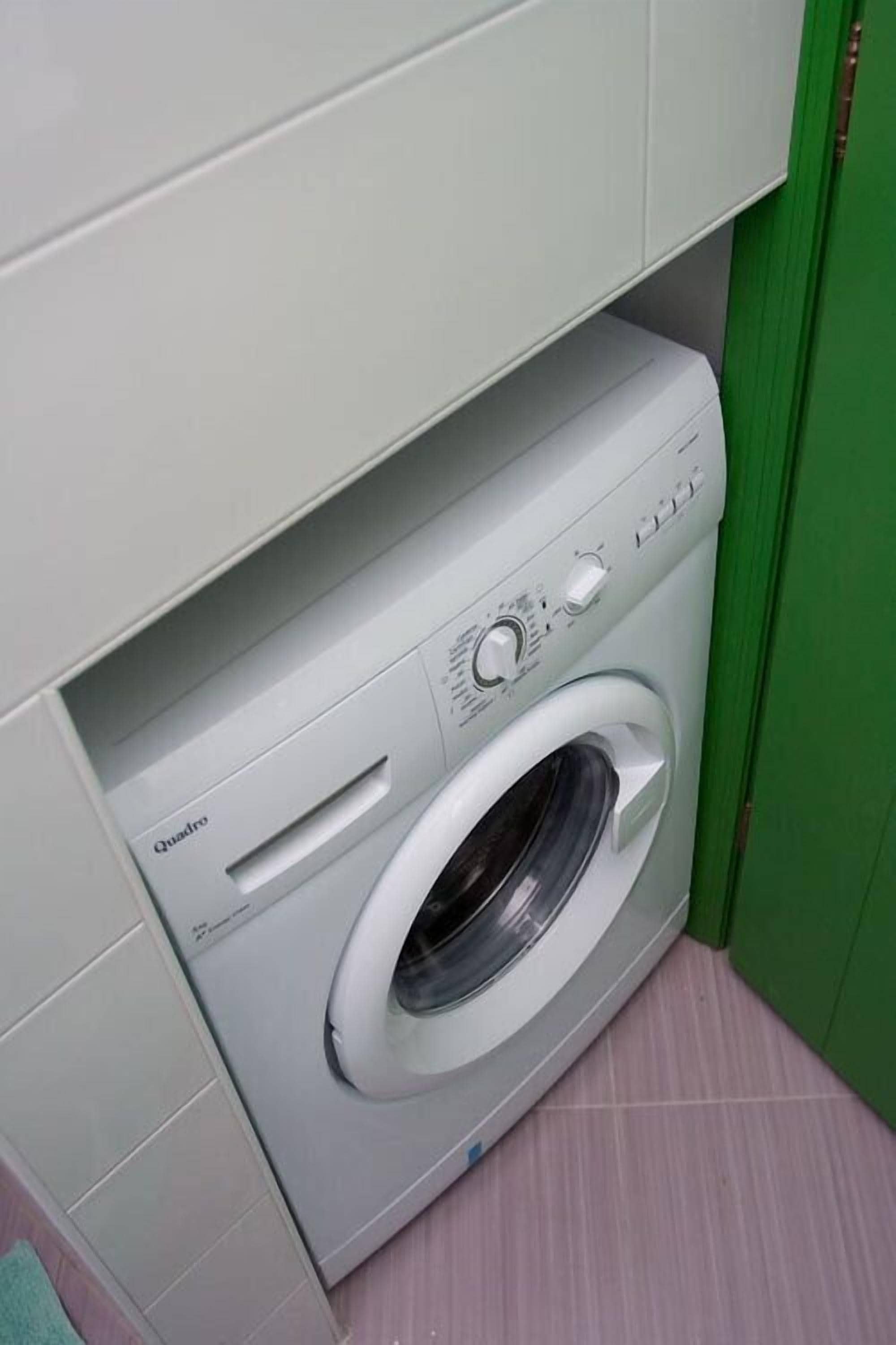 Una lavadora blanca de carga frontal compacta en un lavadero pequeño con una puerta verde.