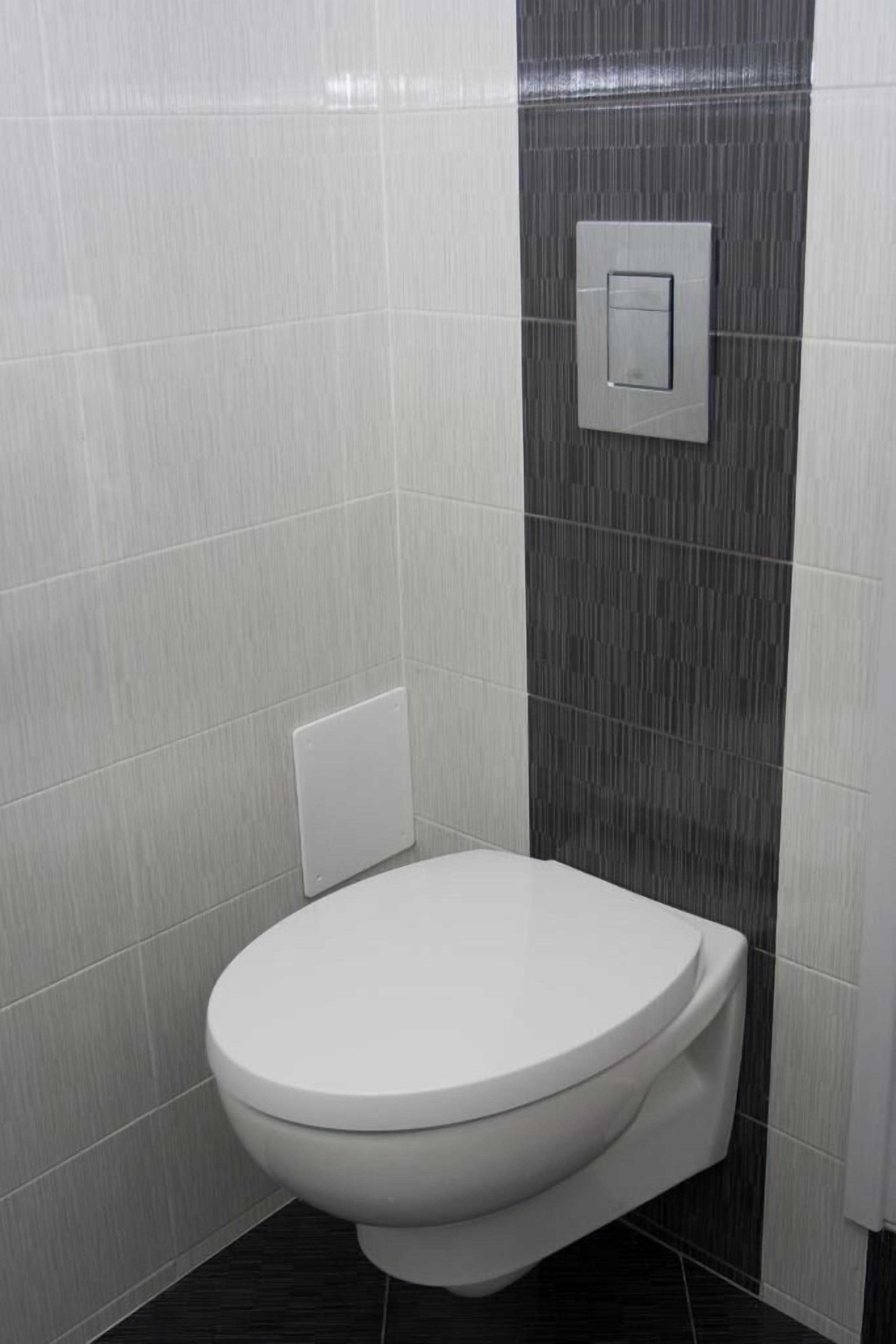 Een compacte, moderne badkamer met een wit toilet, een wandbediend spoelmechanisme en ventilatie.