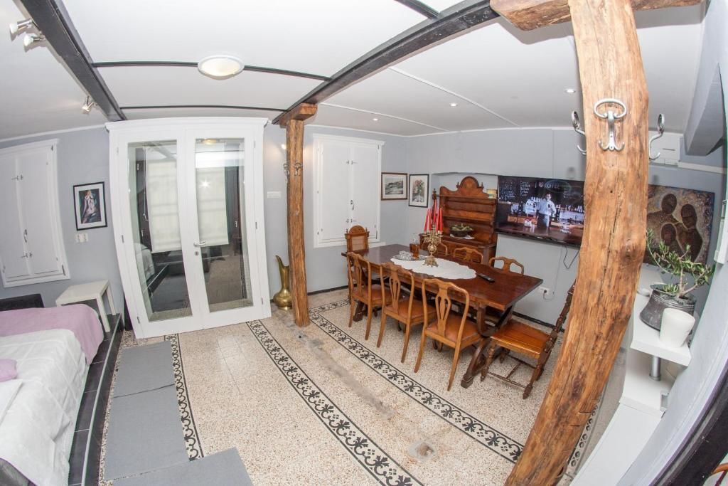 A room with a dining area featuring a wooden table and chairs, a bed with a white headboard, and a door leading to another room.