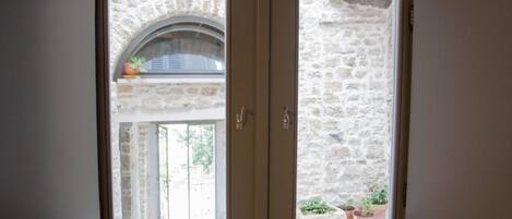 A double door with a stone wall view, a small balcony with plants, and a door handle.