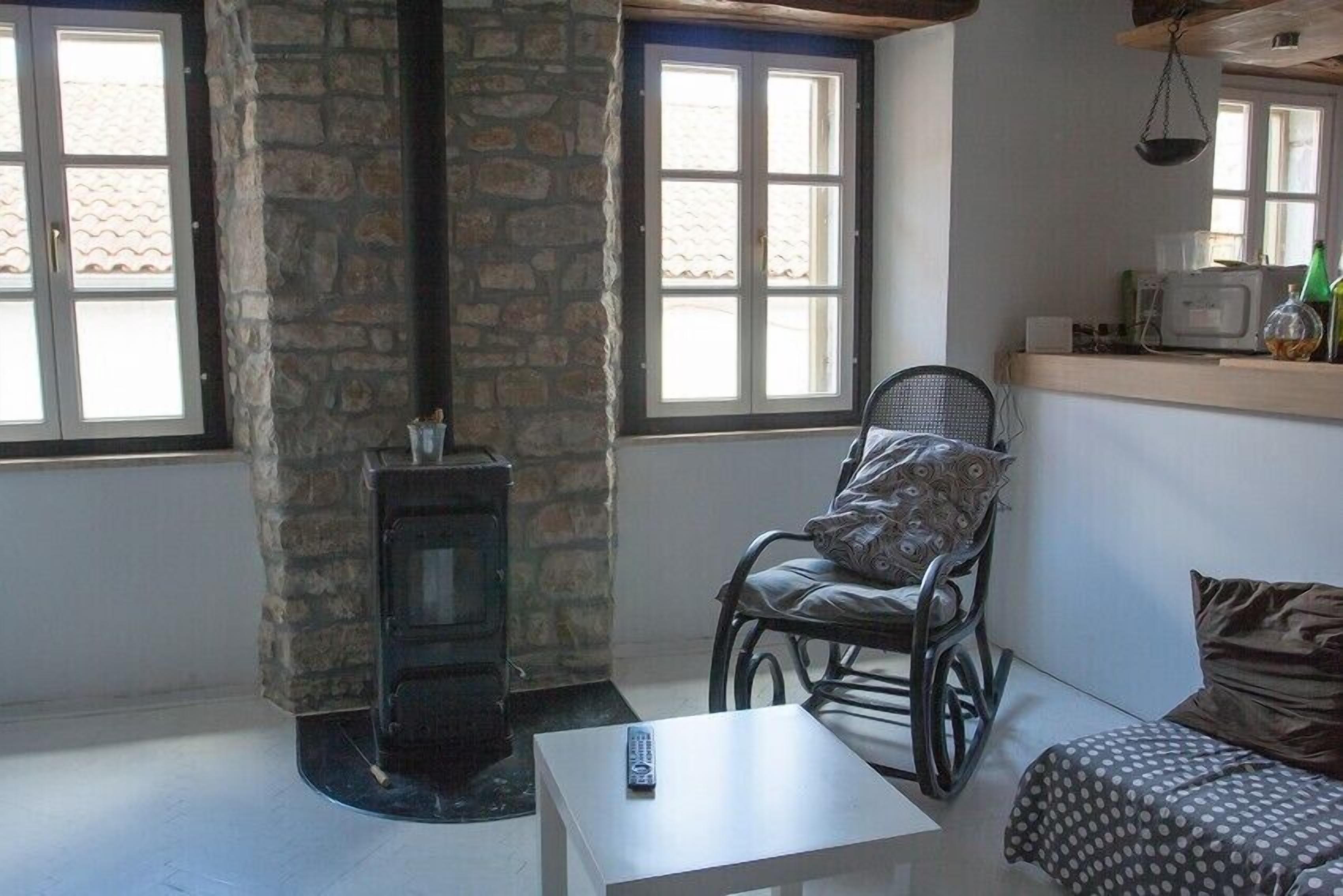 A cozy room with a stone wall, a fireplace, a rocking chair, a small table, and a television on a shelf.