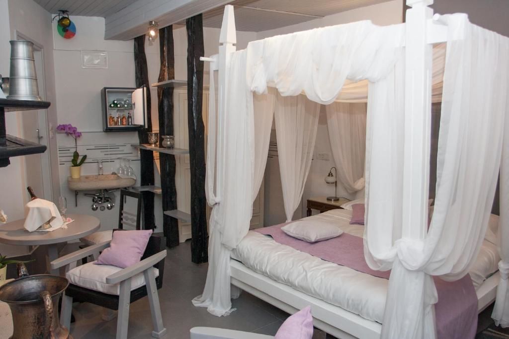 A bedroom with a canopy bed, a round table with chairs, a sink, and a shelf with bottles.
