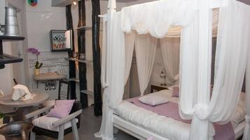 A bedroom with a canopy bed, a round table with chairs, a sink, and a shelf with bottles.