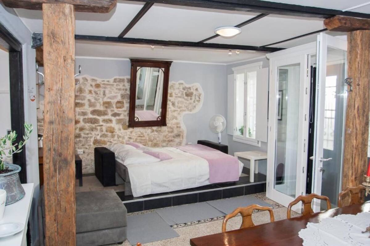 A bedroom with a stone wall, a bed, a bedside table, a chair, and a window.