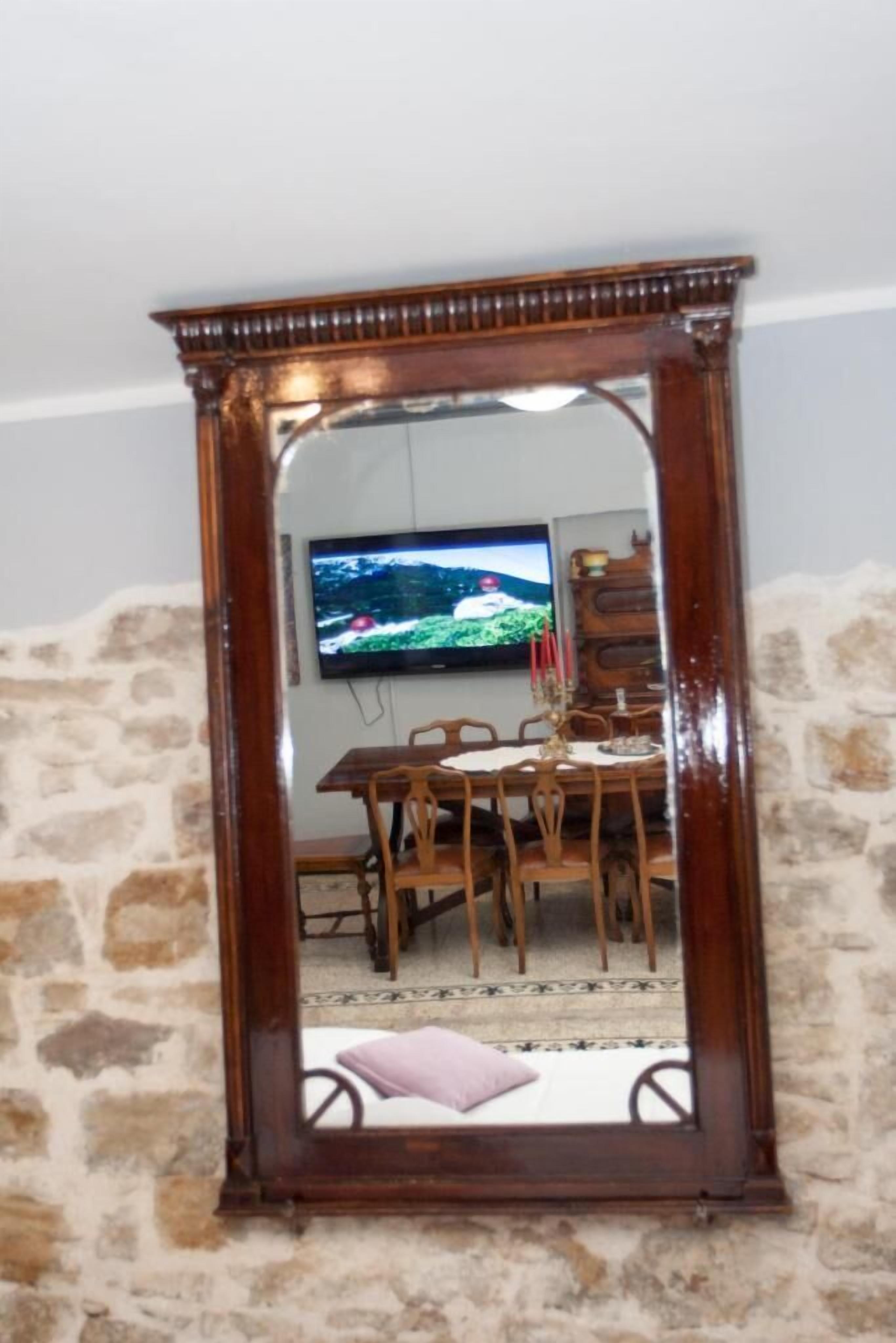 A mirror with a wooden frame reflecting a dining area with a TV mounted on the wall.