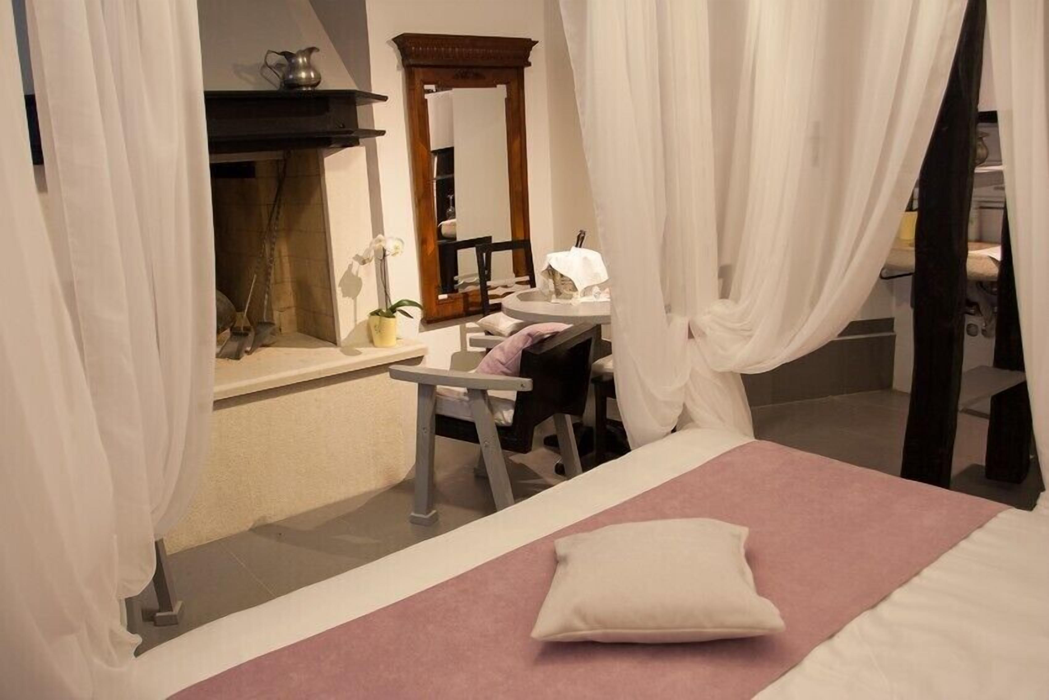 Un dormitorio con cama, mesita de noche, silla, espejo y ventana con cortinas.