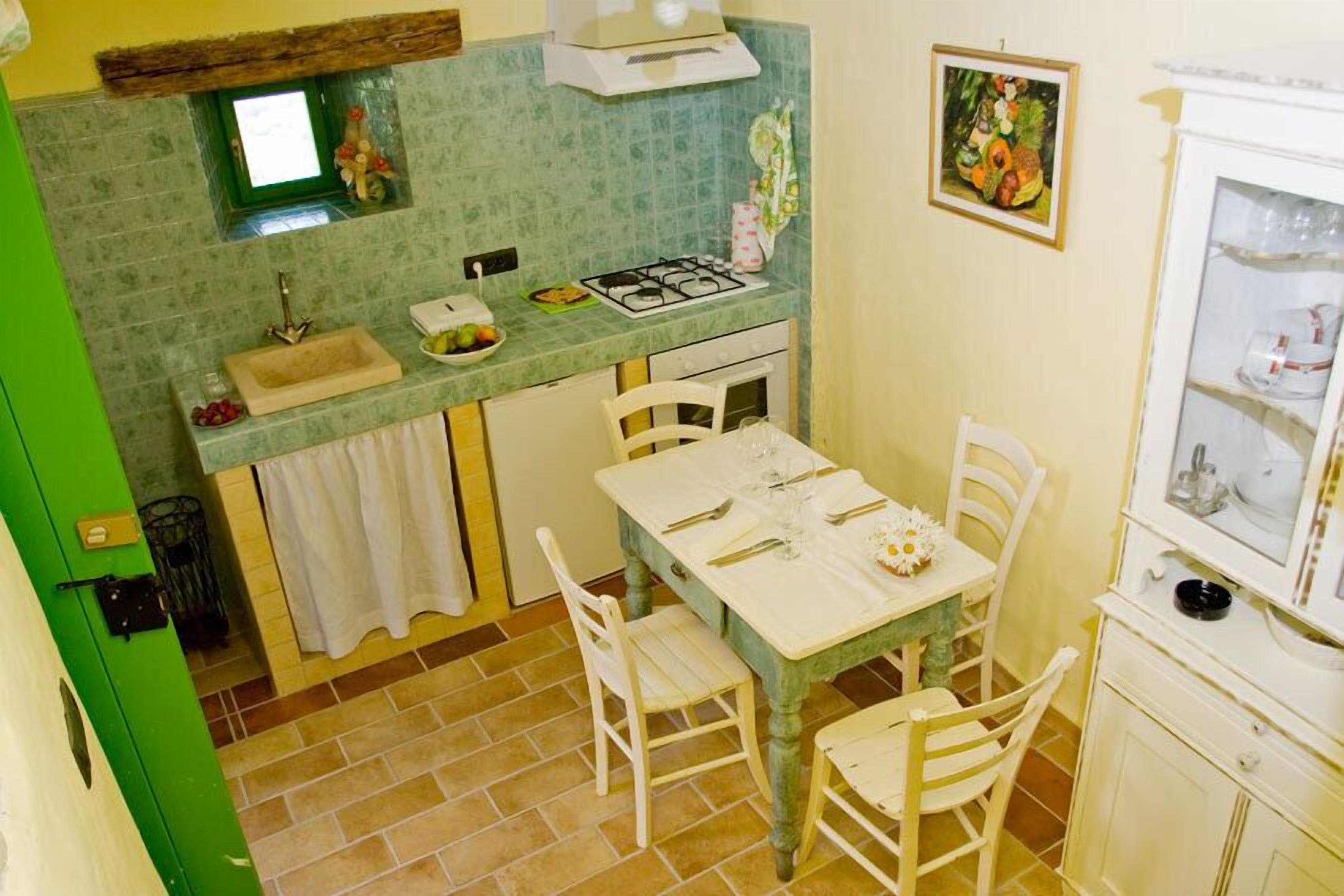 Una cocina con salpicadero de azulejos verdes, un lavabo blanco, una estufa y una mesa de comedor con sillas blancas.