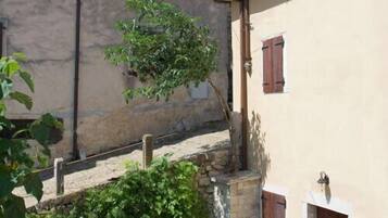 A narrow street with buildings on both sides, featuring stone walls and wooden shutters.
