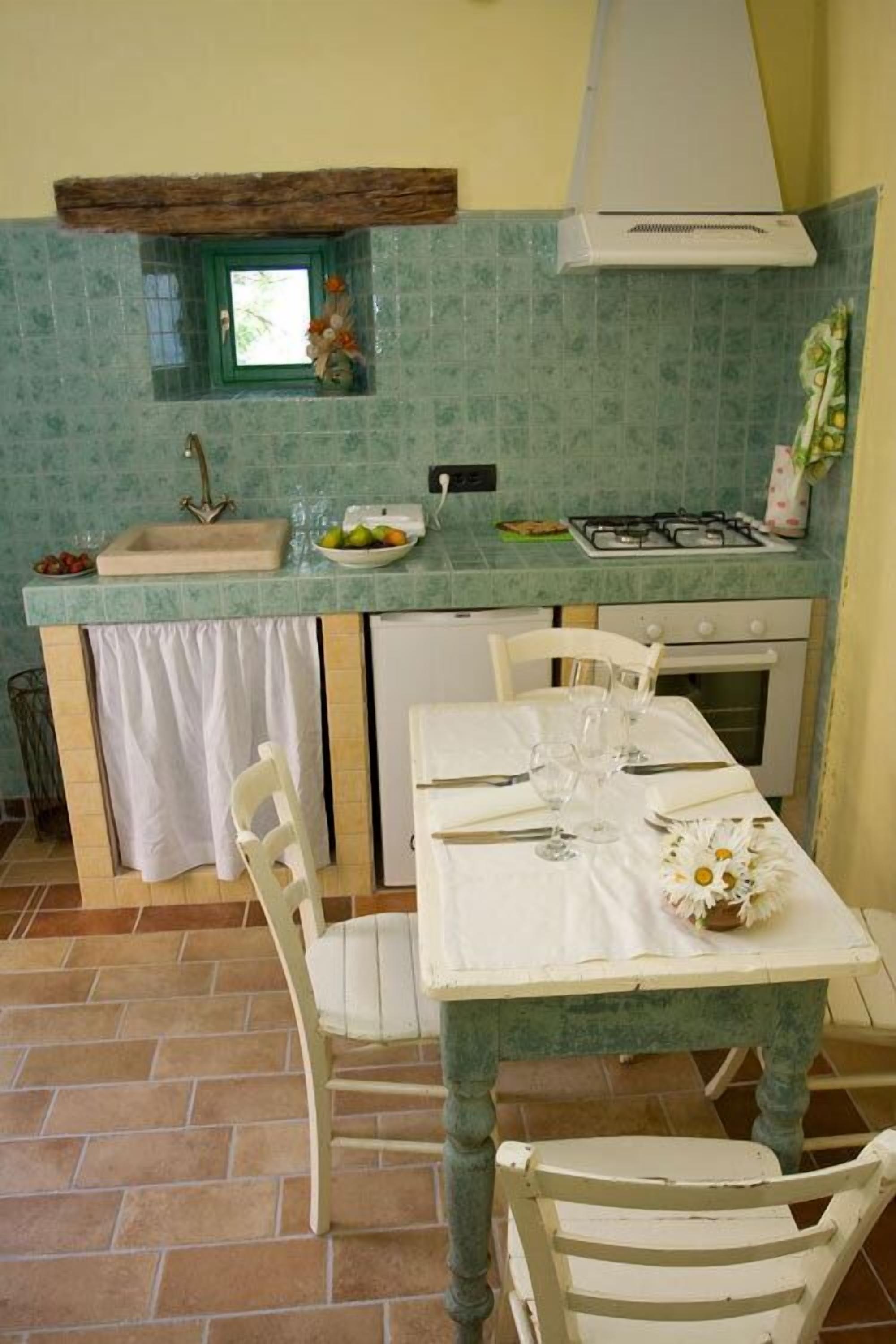 A compact kitchen with a sink, stove, and a small window. There is a dining table with chairs and a vase of flowers.