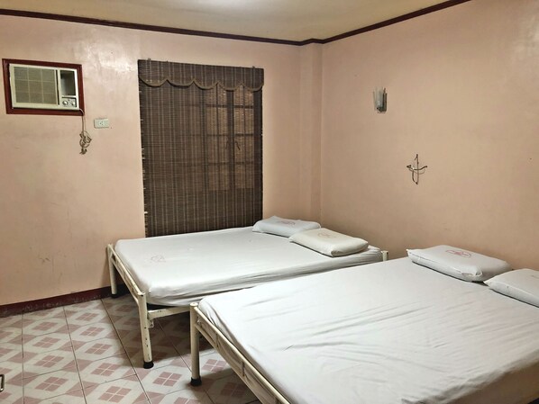 Una habitación con dos camas individuales, una ventana con cortina, un equipo de aire acondicionado y un aplique de pared.