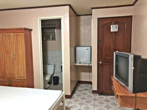 Una habitación con una cama, un armario de madera, un inodoro, un televisor blanco pequeño y una puerta de madera con un cartel.