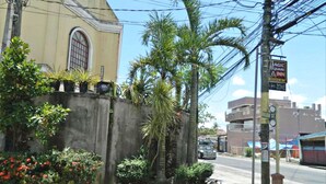 A building with a large arched window, a concrete wall with potted plants, and a street with a sign for 'Magic Square Inn'.