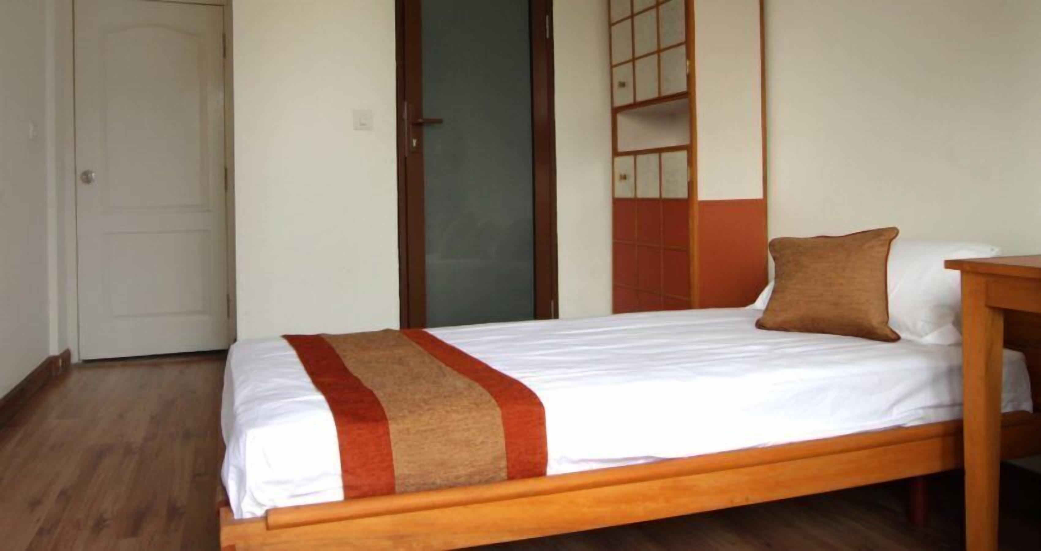 A single bed with a wooden frame, white bedding, and a brown pillow.