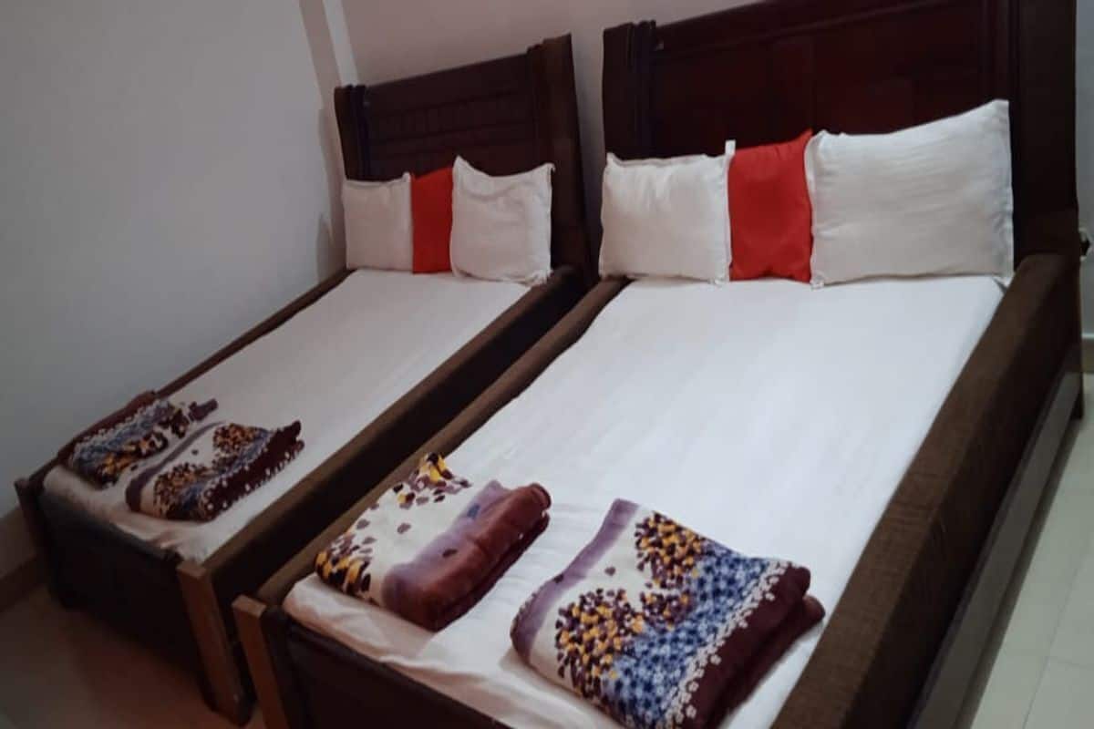 Two single beds with wooden headboards, white linens, and red accent pillows.