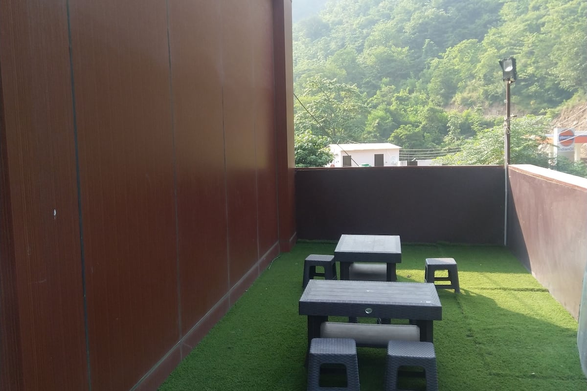 An outdoor patio with artificial grass, a wooden wall, and a view of a green hillside.