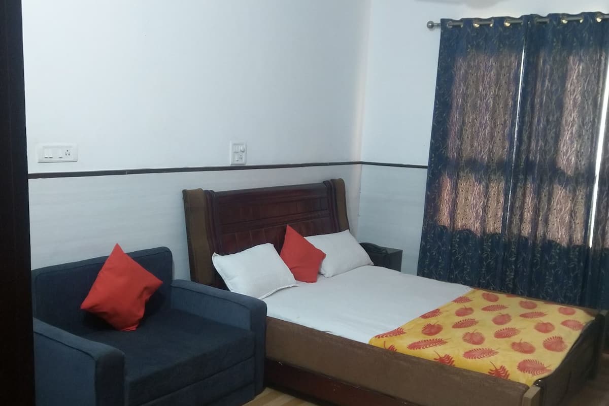 A bedroom with a bed, a sofa, a ceiling fan, and a window with curtains.