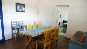 Un coin repas avec une table et des chaises en bois, un tableau encadré au mur et une cuisine en arrière-plan.