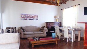 Un salon comprenant un canapé, une table basse, une table à manger avec des chaises, une lampe et un tableau accroché au mur.