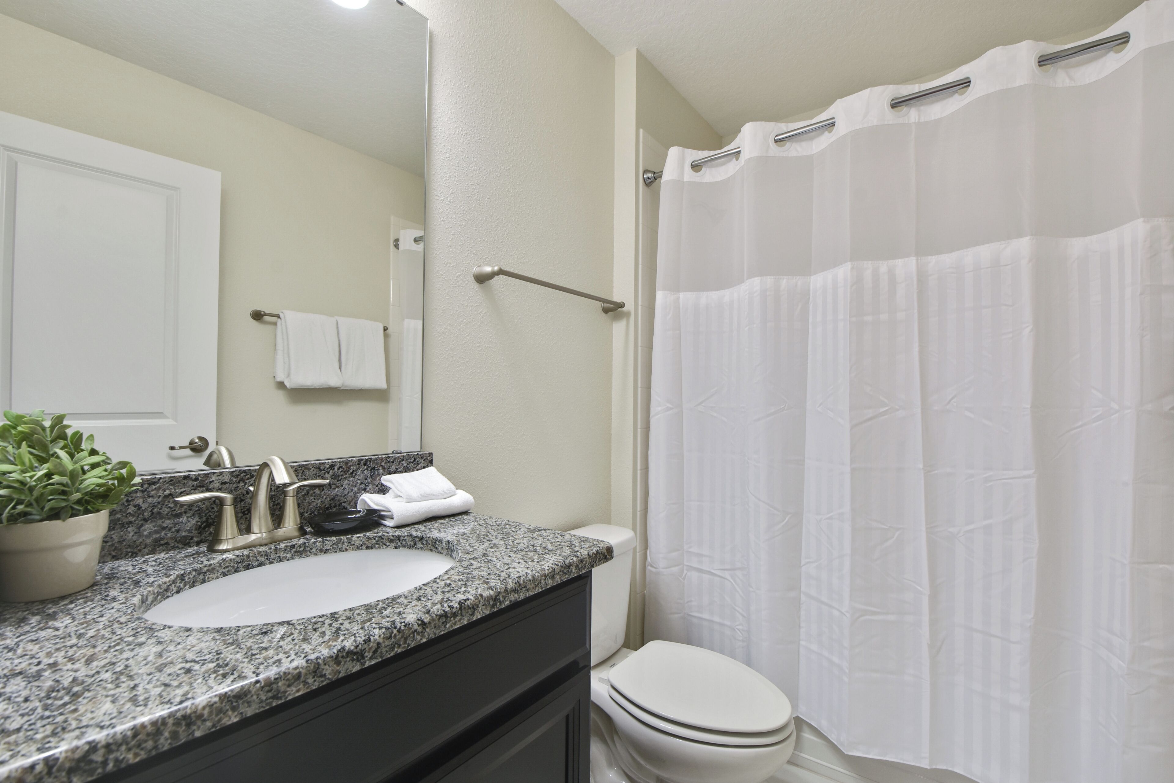 A bathroom with a granite countertop sink, a white toilet, a shower curtain, and a towel rack.