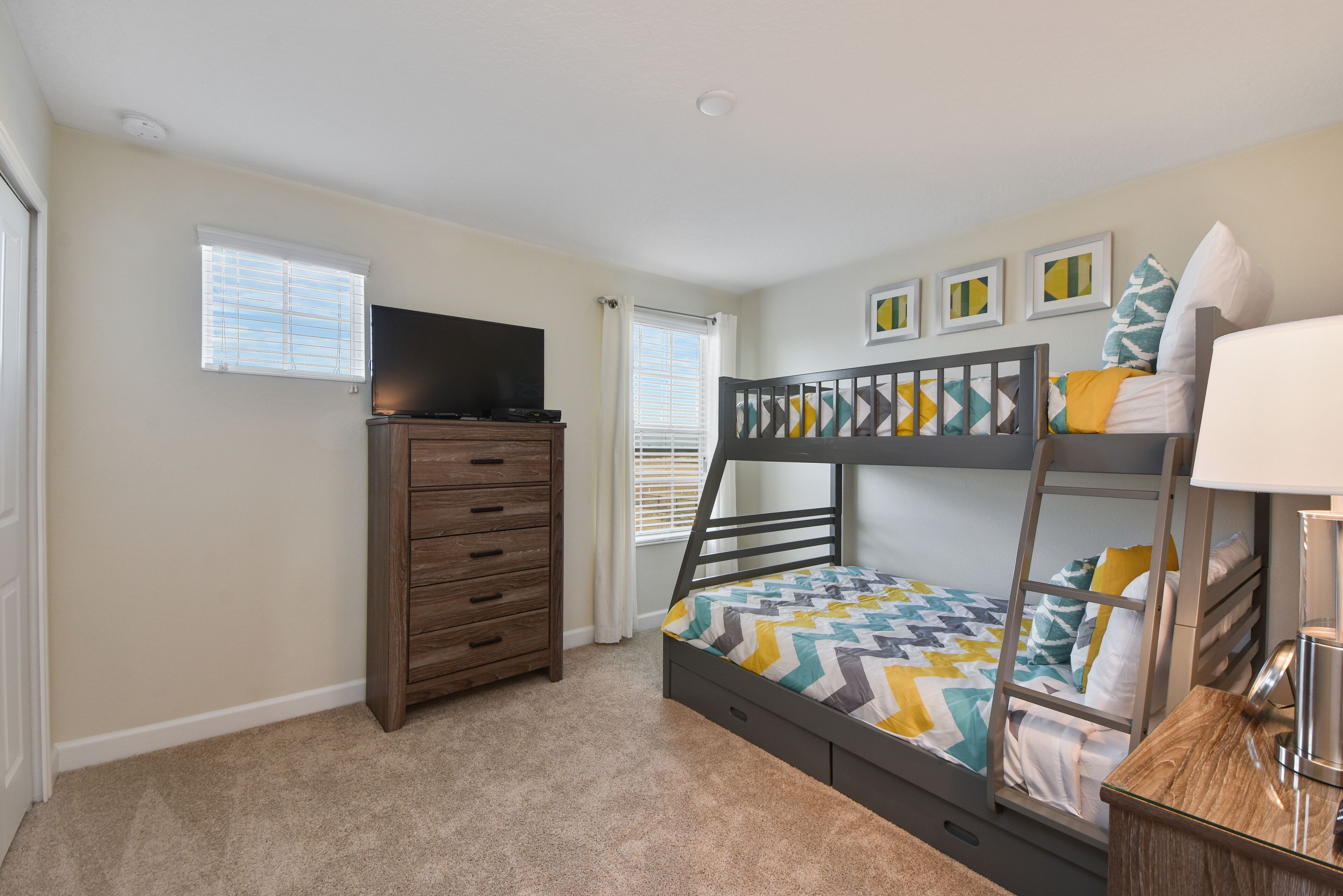 A bedroom with a bunk bed, a dresser, a television, and a window with blinds.