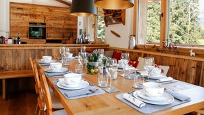 A wooden dining table set with white plates, glasses, and cutlery, with a kitchen in the background.