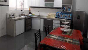 Ett kompakt kök med vita skåp, ett kylskåp i rostfritt stål, en spis och ett matbord med en röd duk.