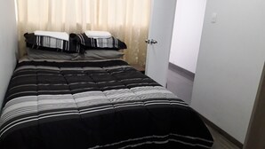 En säng för en person med ett randigt överkast, ett sängbord med en lampa och en dörr till badrummet.