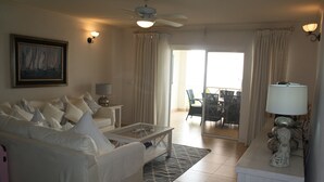 A living room with a white sofa, a coffee table, a ceiling fan, and a view of the balcony.