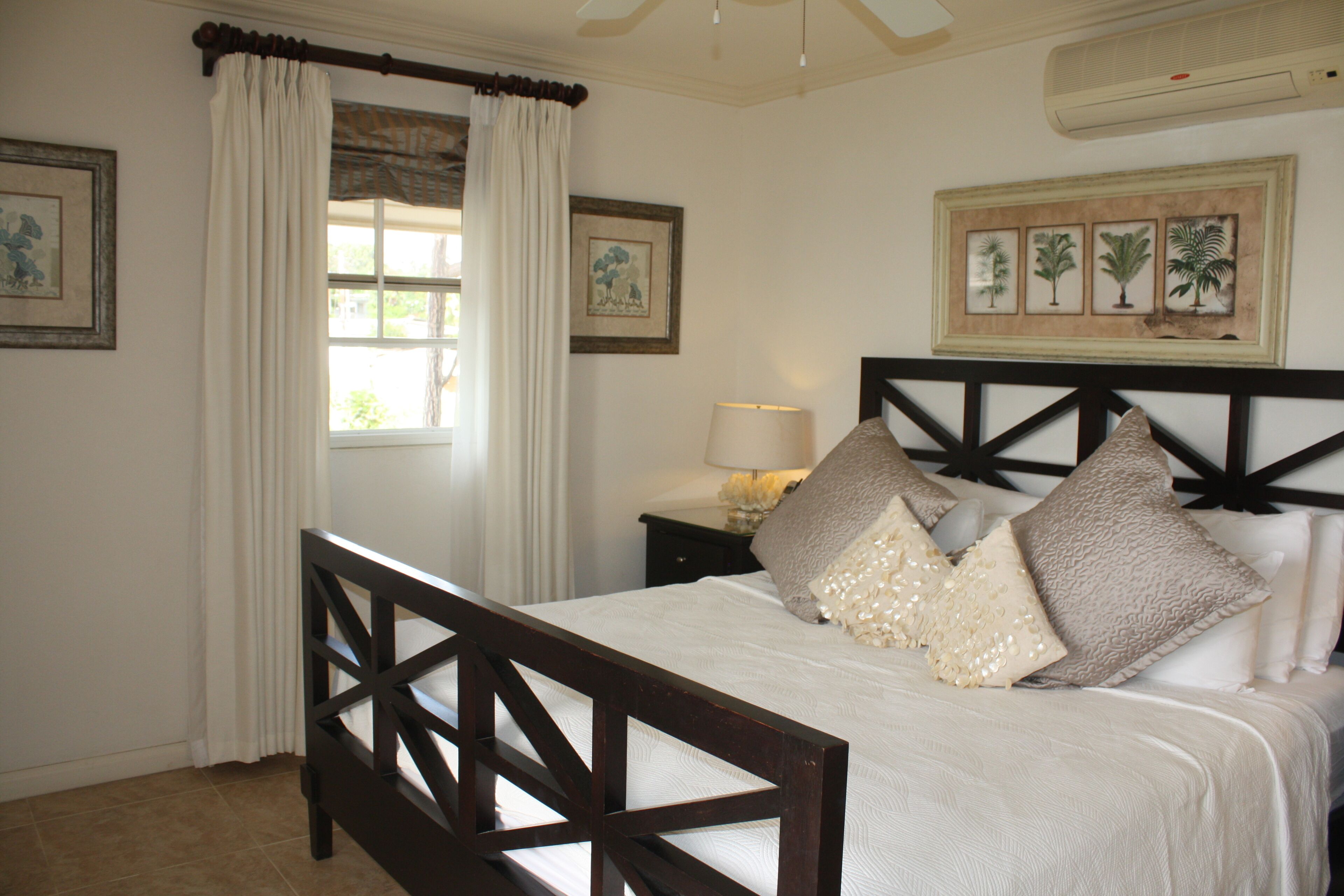 A neatly made bed with a wooden headboard, a bedside table with a lamp, and a window with curtains.