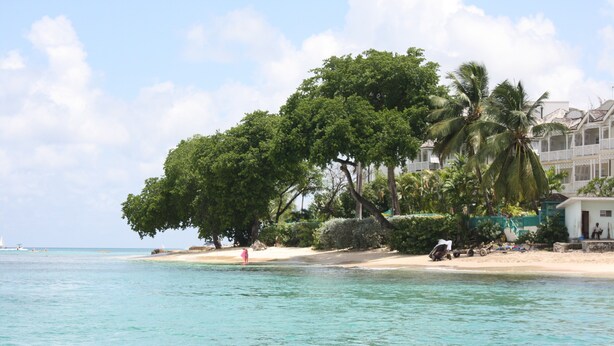 A beach with clear turquoise water, palm trees, and a building with a balcony.